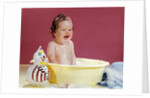 1960s crying brunette baby sitting in yellow plastic bath tub with toy clown by Anonymous