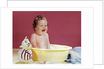 1960s crying brunette baby sitting in yellow plastic bath tub with toy clown by Anonymous