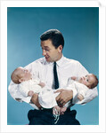 1960s father holding twin babies infants looking down at one of them by Anonymous