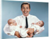 1960s smiling man father looking at camera holding twin babies infants by Anonymous