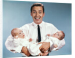 1960s smiling man father looking at camera holding twin babies infants by Anonymous