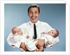 1960s smiling man father looking at camera holding twin babies infants by Anonymous