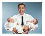 1960s smiling man father looking at camera holding twin babies infants by Anonymous
