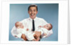 1960s smiling man father looking at camera holding twin babies infants by Anonymous