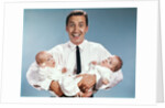 1960s smiling man father looking at camera holding twin babies infants by Anonymous