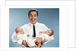 1960s smiling man father looking at camera holding twin babies infants by Anonymous