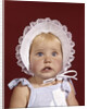 1960s portrait baby girl wearing bonnet and blue gingham dress showing two front teeth looking at camera by Anonymous