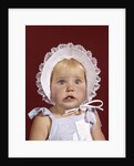 1960s portrait baby girl wearing bonnet and blue gingham dress showing two front teeth looking at camera by Anonymous