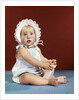 1960s baby girl ruffled bonnet holding bottle funny facial expression looking at camera by Anonymous