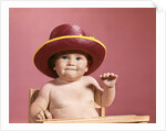 1960s baby making face wearing red straw hat by Anonymous