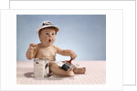 1960s baby with funny facial expression wearing painters cap holding paintbrush sitting by paint can by Anonymous