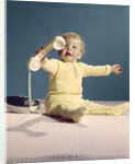1960s baby holding telephone head set by Anonymous