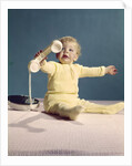 1960s baby holding telephone head set by Anonymous
