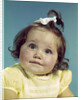 1960s brunette baby girl round chubby face yellow dress ribbon topknot interested sincere facial expression looking at camera by Anonymous