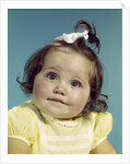 1960s brunette baby girl round chubby face yellow dress ribbon topknot interested sincere facial expression looking at camera by Anonymous