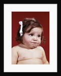 1960s portrait of chubby unhappy baby girl with white ribbon bow in messy hair by Anonymous