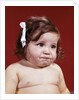 1960s portrait of chubby unhappy baby girl with white ribbon bow in messy hair by Anonymous