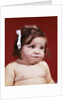 1960s portrait of chubby unhappy baby girl with white ribbon bow in messy hair by Anonymous