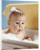 1960s baby with a surprised facial expression in bathtub covered with soap bubbles by Anonymous