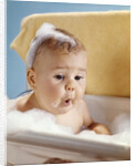 1960s baby with a surprised facial expression in bathtub covered with soap bubbles by Anonymous