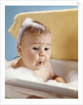 1960s baby with a surprised facial expression in bathtub covered with soap bubbles by Anonymous