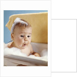1960s baby with a surprised facial expression in bathtub covered with soap bubbles by Anonymous