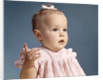 1960s baby girl wearing pink dress with a bow in her hair pointing a finger by Anonymous