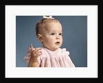 1960s baby girl wearing pink dress with a bow in her hair pointing a finger by Anonymous