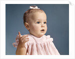 1960s baby girl wearing pink dress with a bow in her hair pointing a finger by Anonymous