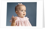 1960s baby girl wearing pink dress with a bow in her hair pointing a finger by Anonymous