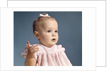1960s baby girl wearing pink dress with a bow in her hair pointing a finger by Anonymous