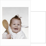 1960s 1970s smiling baby wearing bib and holding wooden spoon by Anonymous
