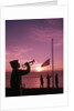 1960s boy scout blowing bugle as others raise american flag at camp sunset ceremony by Anonymous