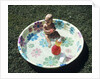 1970s baby sitting in plastic backyard kiddy pool viewed from above by Anonymous
