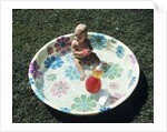 1970s baby sitting in plastic backyard kiddy pool viewed from above by Anonymous