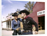 1960s cowboy sheriff with badge draws gun arrests gunfighter in front of livery stable by Anonymous