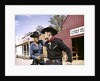 1960s cowboy sheriff with badge draws gun arrests gunfighter in front of livery stable by Anonymous