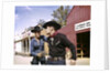 1960s cowboy sheriff with badge draws gun arrests gunfighter in front of livery stable by Anonymous