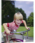 1970s 1960s smiling blond boy leaning over handlebars of bicycle looking at camera by Anonymous