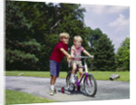 1960s 1970s boy helping little brother ride two wheel bicycle with training wheels by Anonymous