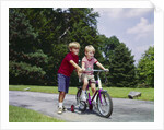 1960s 1970s boy helping little brother ride two wheel bicycle with training wheels by Anonymous