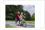 1960s 1970s boy helping little brother ride two wheel bicycle with training wheels by Anonymous