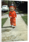 1950s little boy in red outfit running on pavement with mother just behind by Anonymous