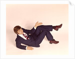 1970s overhead looking down at man lying down legs crossed wearing business suit shrug off hand expression looking at camera by Anonymous