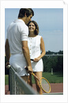 1970s smiling couple standing by net on tennis court holding wood rackets by Anonymous