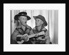 1950s 2 juvenile boys in cowboy hat & shirts playing ukulele & singing mouth open wide by Anonymous