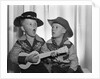 1950s 2 juvenile boys in cowboy hat & shirts playing ukulele & singing mouth open wide by Anonymous