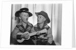 1950s 2 juvenile boys in cowboy hat & shirts playing ukulele & singing mouth open wide by Anonymous