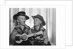 1950s 2 juvenile boys in cowboy hat & shirts playing ukulele & singing mouth open wide by Anonymous