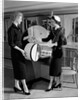 1950s woman in hat stole & gloves taking hatbox from saleswoman by Anonymous